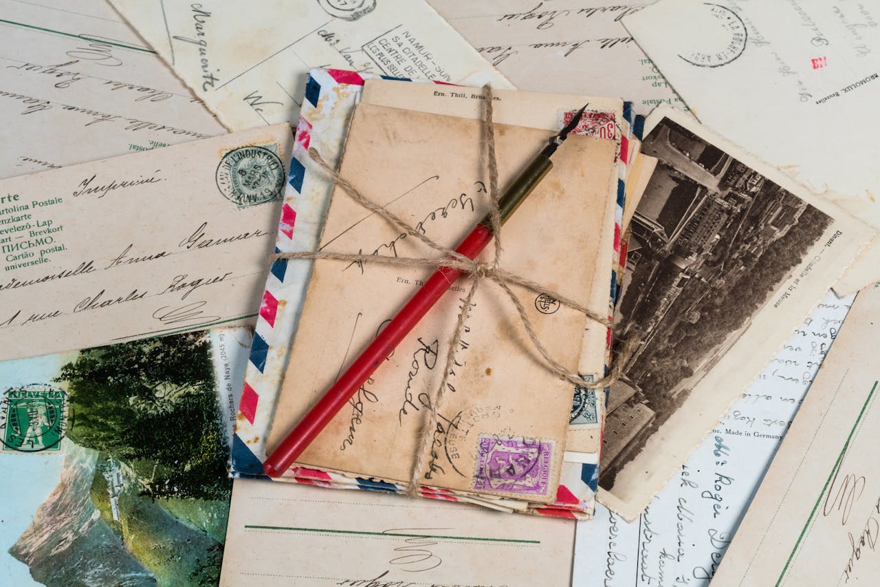 A collection of vintage postcards and envelopes tied with twine, featuring a pen and old stamps.